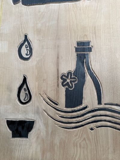 手彫りのロゴ板(酒の字に見立てた瓶と杯の絵)