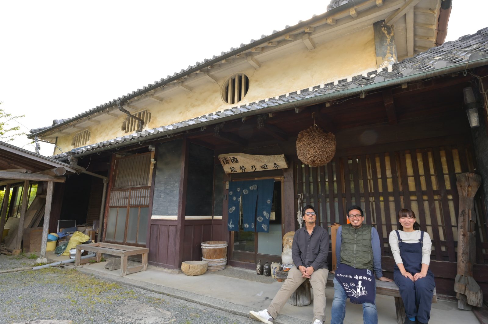築130年の古民家店舗の前に座る三人のスタッフ